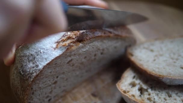 Primer plano de las manos rebanando pan crujiente con cuchillo afilado en una tabla de madera. — Vídeos de Stock