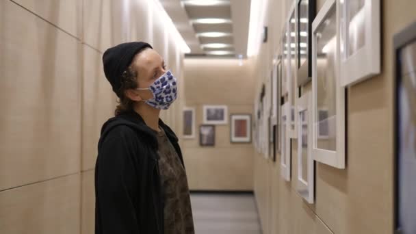 Jonge vrouw met gezichtsmasker kijkend naar foto 's in fotogalerij. Educatieve activiteiten tijdens de covid-19 pandemie — Stockvideo