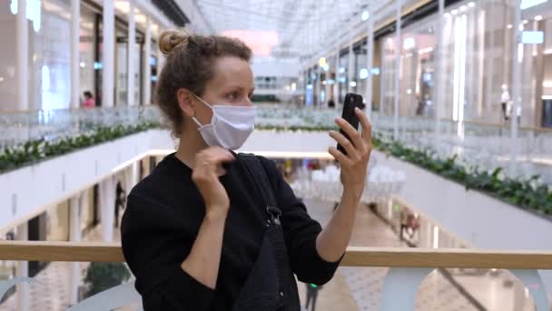 Donna con maschera facciale avendo video chat nel centro commerciale durante covid-19 pandemia — Video Stock