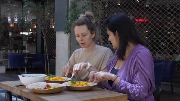 Szőke és barna lányok együtt vacsoráznak. Barátok beszélgetnek egészséges és színes étkezés padláson stílusú étterem. — Stock videók