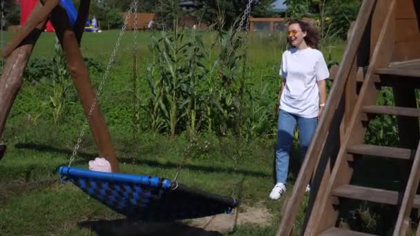 Divertimento al parco giochi. Mamma single con due bambini gemelli che godono di grandi altalene per più bambini — Video Stock