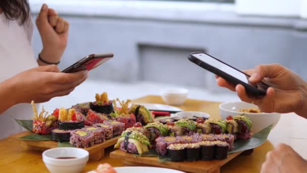 Två personer tar bilder på sina färgglada veganska sushi set med smartphones under lunchen. Friska vegan livsstil koncept — Stockvideo