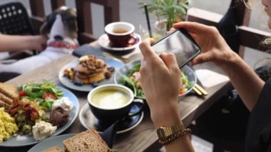 Şehir kafesinde akıllı telefonla sağlıklı vejetaryen brunch 'ı çeken bir kız. Gıda bloglama kavramı