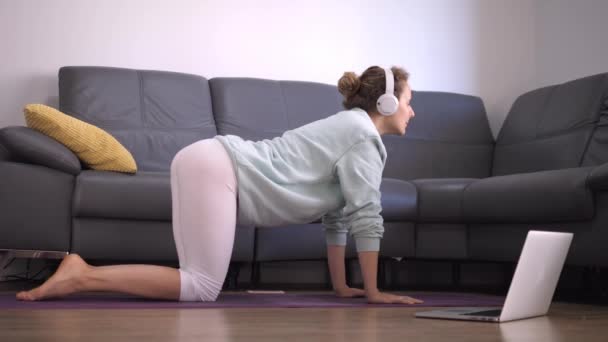 Seitenansicht einer jungen Frau, die Yoga zu Hause über eine Online-Plattform praktiziert. Selbstisolation während der Covid-19-Pandemie — Stockvideo