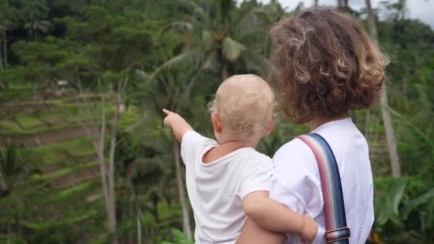 Rückenansicht einer kaukasischen Frau, die ihr Baby hält und auf die Dschungel-Landschaft blickt. — Stockvideo