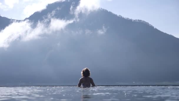 Vista trasera de una silueta de una mujer saltando de las aguas termales naturales de Batur. Batur montaña en la parte posterior — Vídeo de stock