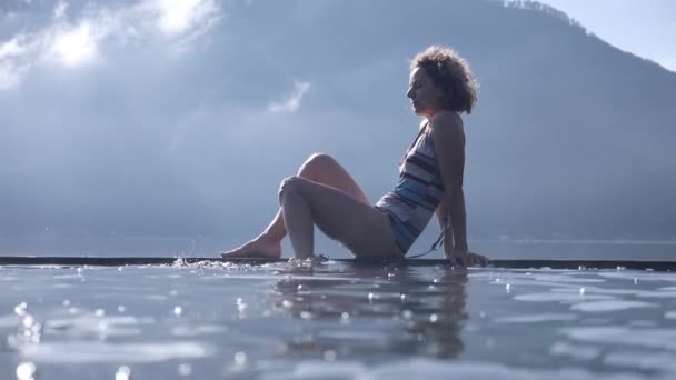 Batur natürliche Thermalquellen. Seitenansicht einer Frau, die vor dem Batur-Berg mit ihren Beinen Wasser spritzt — Stockvideo