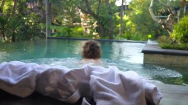 Lüks tatil köyünde sabah ayinleri. Yüzme havuzunda çıplak yüzen bir kadın