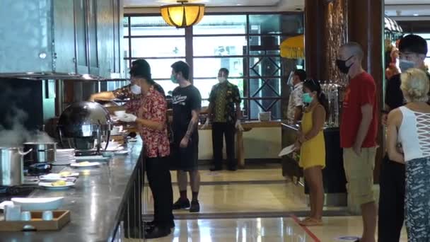 Büfé a hotelben. Az arcmaszkos vásárlók sorban állnak az ételért. Bali-December-2020 — Stock videók