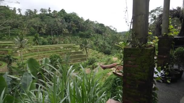 Balinesische Reisfelder. Frau mittleren Alters auf einer hölzernen Schaukel alter Schule — Stockvideo