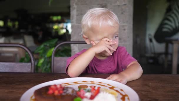 Симпатична маленька втомлена біла дитина не хоче їсти млинці з фруктами і вершками — стокове відео