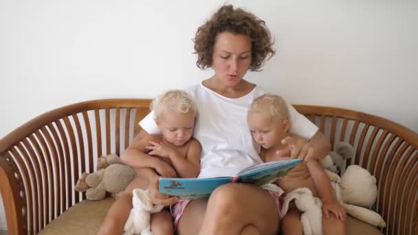 Glücklich liebende Familie Konzept. Hübsche junge kaukasische Mutter liest ihren Zwillingsbabys auf der Couch ein Buch vor — Stockvideo