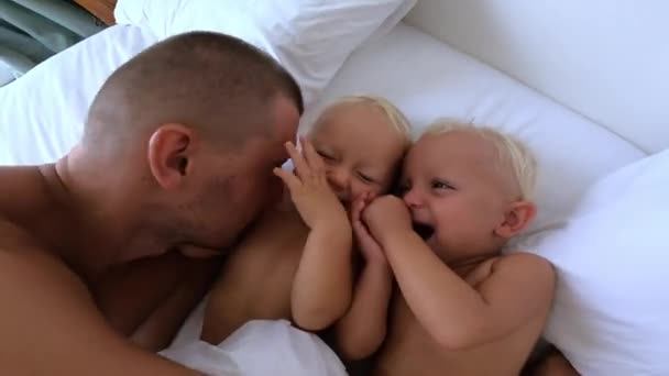 Sevgi dolu bir babanın ikiz bebeklerini yatakta kucaklaması. Mutlu ailede sabah ritüelleri — Stok video