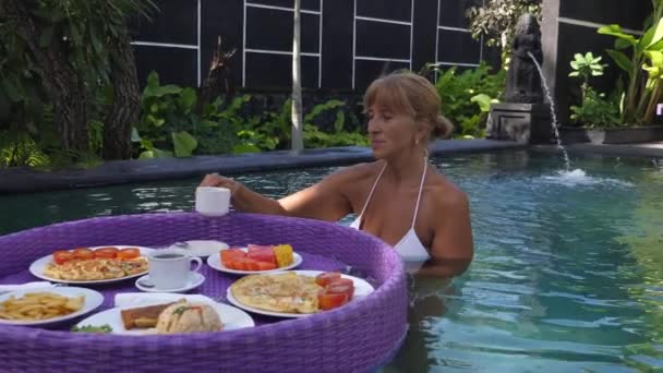 Una mujer de mediana edad en una piscina tomando un desayuno flotante. Vida después de la jubilación — Vídeo de stock