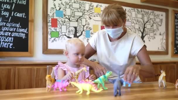 Ausbildungszeit während der Covid-19-Pandemie. Dame in den Gesichtsmasken spielt mit Tierspielzeug mit ihrem kleinen Mädchen — Stockvideo