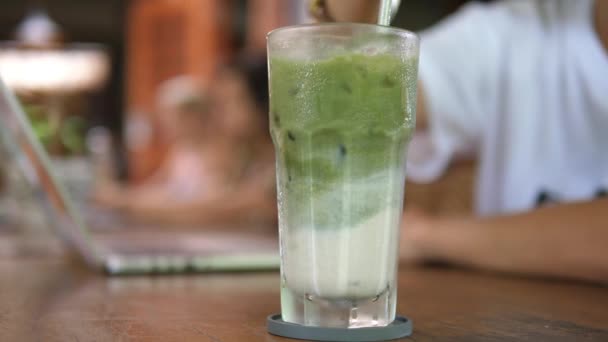 Close up of metal straw stirring matcha ice tea latte with almond milk. Refreshing plant based drinks — Stock Video
