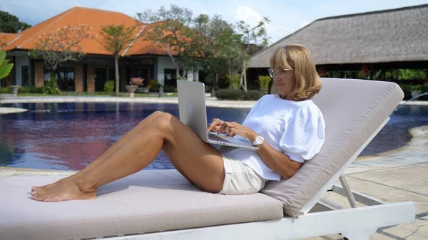 Деловая леди в отпуске. Женщина средних лет работает онлайн у бассейна своей виллы — стоковое фото