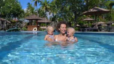 Çocuklarla seyahat etmek kolay ve eğlenceli. Genç anne yüzme havuzunda ikiz kızlarına sarılıyor.