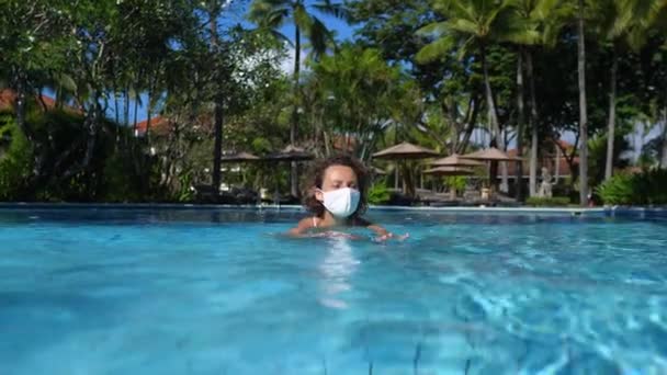 Voyager pendant une pandémie de covidé-10. Femme en masque de protection nageant dans sa piscine. — Video