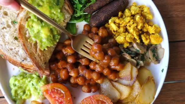 Widok z góry tradycyjne angielskie śniadanie w opcji wegańskiej. Widelec bierze fasolę i pokazuje ją przed kamerą. — Wideo stockowe