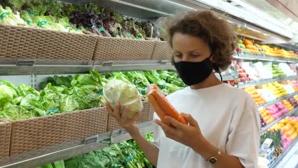 En kvinna i ansiktsmask som jämför noggrant färdigförpackade grönsaker och väljer ut de bästa. Matinköp under covid-19-pandemin. — Stockvideo