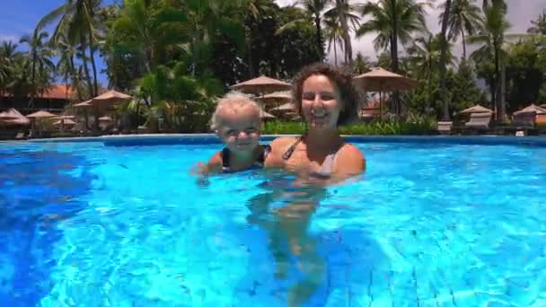Primeros intentos de nadar. Joven madre enseña a su bebé a nadar en una piscina mientras está de vacaciones — Vídeo de stock
