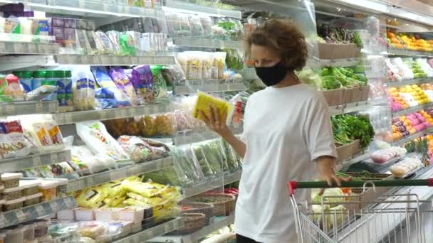 Nő egy arc maszk egy szupermarketben kiválasztja termékeket vásárolni. Békés korlátozások a nyilvános helyeken — Stock videók