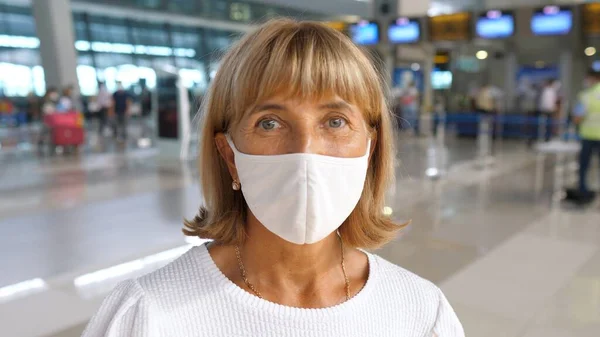 Портрет женщины средних лет в маске для лица, стоящей в аэропорту и смотрящей в камеру. Концепция психического здоровья — стоковое фото
