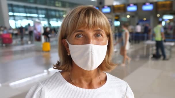 Retrato de una mujer de mediana edad con una máscara facial de pie en el aeropuerto mirando a la cámara. Concepto de salud mental — Vídeos de Stock
