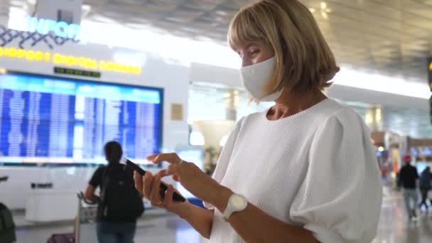 Mujer con una máscara facial en el aeropuerto revisando la hora de su reloj para no perder su vuelo. — Vídeo de stock