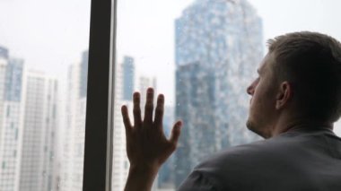Sosyalleşme özlemi çeken bir adamın kafasını pencereye dayamasının arkası. Arkaplanda gökdelenler