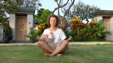 Genç Kafkasyalı kadın bir bahçede nilüfer pozisyonunda otururken bebeğini emziriyor. 