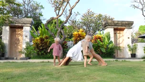 Divertido tiempo en familia afuera. Mamá enseña a sus bebés gemelos a practicar yoga en un jardín tropical — Vídeo de stock