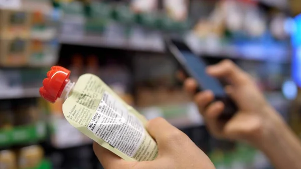 Bir elin püre tutarken diğerinin arka planında akıllı telefon kullanarak kapat. Bebek maması alışverişi.