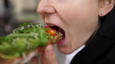 Kafkasyalı bir kızın sağlıklı bir avokado tostundan büyük bir iştahla bir ısırık almasına yakından bakın.. 