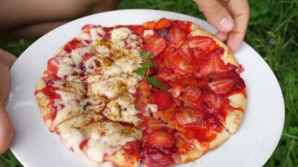 O mână care culege o felie de pizza vegană acoperită cu brânză și căpșuni fără lapte. Hipster pe bază de plante alimente de stradă — Videoclip de stoc