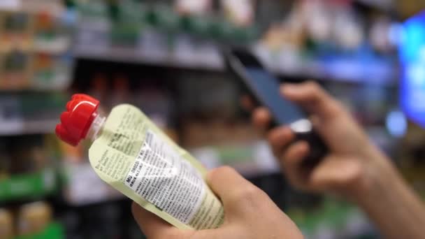 Közelkép egy kéz gazdaság püré és a második a háttérben segítségével okostelefon. Vásárlás bébiétel-koncepció — Stock videók