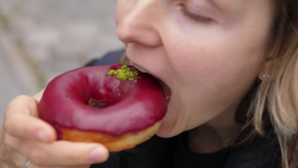 Close up of a hungry woman taking a bite of berry vegan doughnut with her eyes closed. — Stock Video