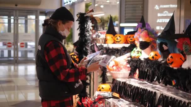 Mujer joven en una máscara de la cara de compras para las decoraciones de Halloween. Compras durante la pandemia de covid-19 — Vídeos de Stock