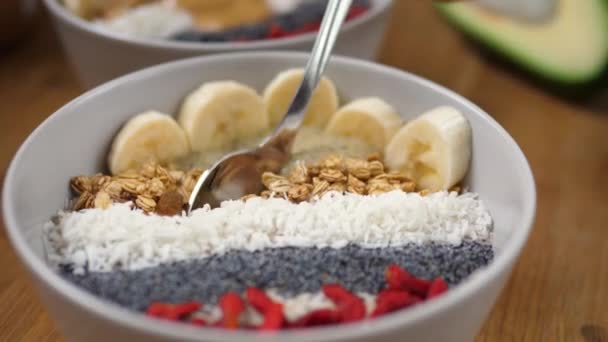 Concepto de desayunos a base de plantas. Cuchara se sumerge en un batido cremoso dulce cubierto con plátano y granola y lo muestra en la cámara — Vídeo de stock