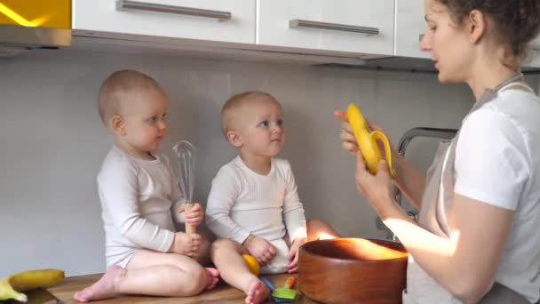 Jeune Multitâche mère nourrit banane ses bébés jumeaux tout en faisant un dîner — Video