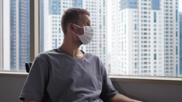 Kontoret kämpar för att arbeta hemifrån ensam på grund av koronavirus. En upprörd man vid fönstret i en skyddande ansiktsmask — Stockvideo
