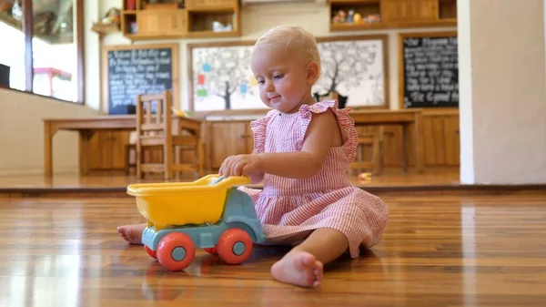 白人幼児女の子遊びますおもちゃの車と恐竜で保育園 — ストック写真