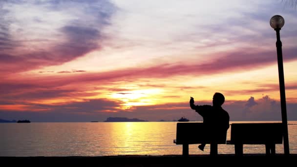 Mann sitzt am Strand und fotografiert den schönen Sonnenuntergang. — Stockvideo