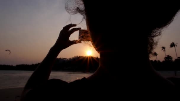 Жінка за допомогою смарт-телефон сфотографувати на пляжі на заході сонця. — стокове відео