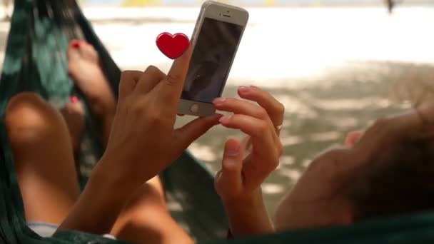 Женщина с помощью смартфона в Hammock и летающей анимации 3D сердца иконки с устройства. Нравится? . — стоковое видео