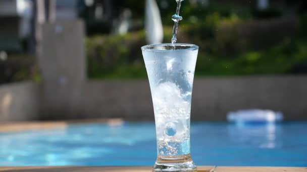 Acqua che scorre nel vetro con ghiaccio vicino alla piscina. Rallentatore . — Video Stock
