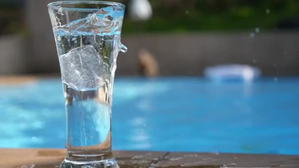 Is kuber faller i glas av vatten nära poolen. Slow Motion. — Stockvideo