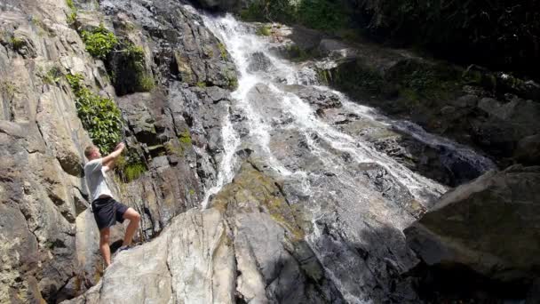 Young Man Taking Photo of Waterfall by Mobile Phone Outdoors — Wideo stockowe