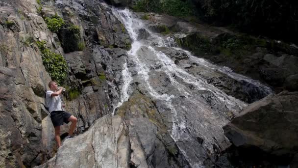 Dorstige sport man met een pauze drink water bij waterval. Slow Motion. — Stockvideo